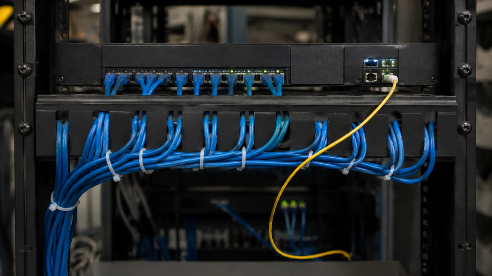 Rack de rede com cabo de fibra óptica organizado entre conversor de mídia e switch