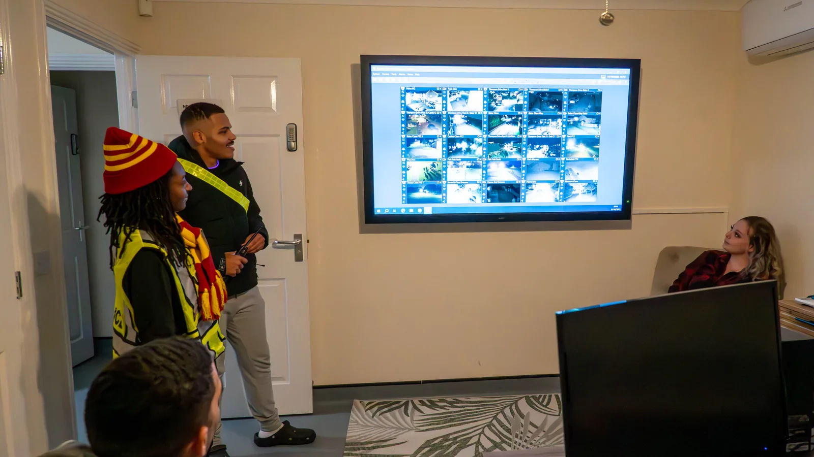 Pessoas observando um painel com grade de imagens de várias câmeras de segurança em uma tela grande