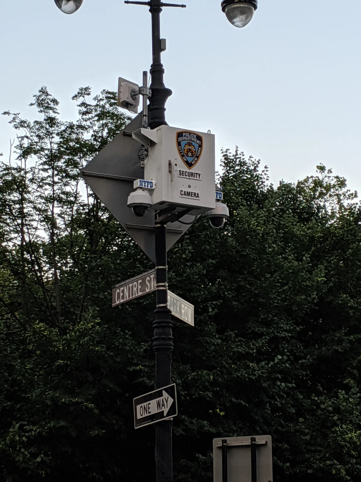 Câmeras de vigilância urbana montadas em poste de rua, com placas de sinalização de trânsito abaixo