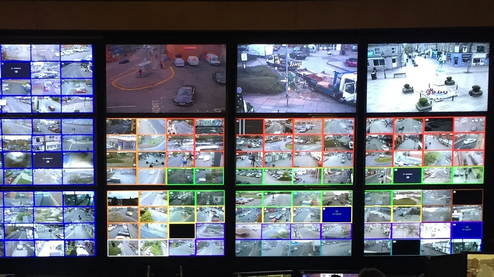 Parede com dezenas de monitores exibindo imagens de câmeras de vigilância urbana em uma central de operações