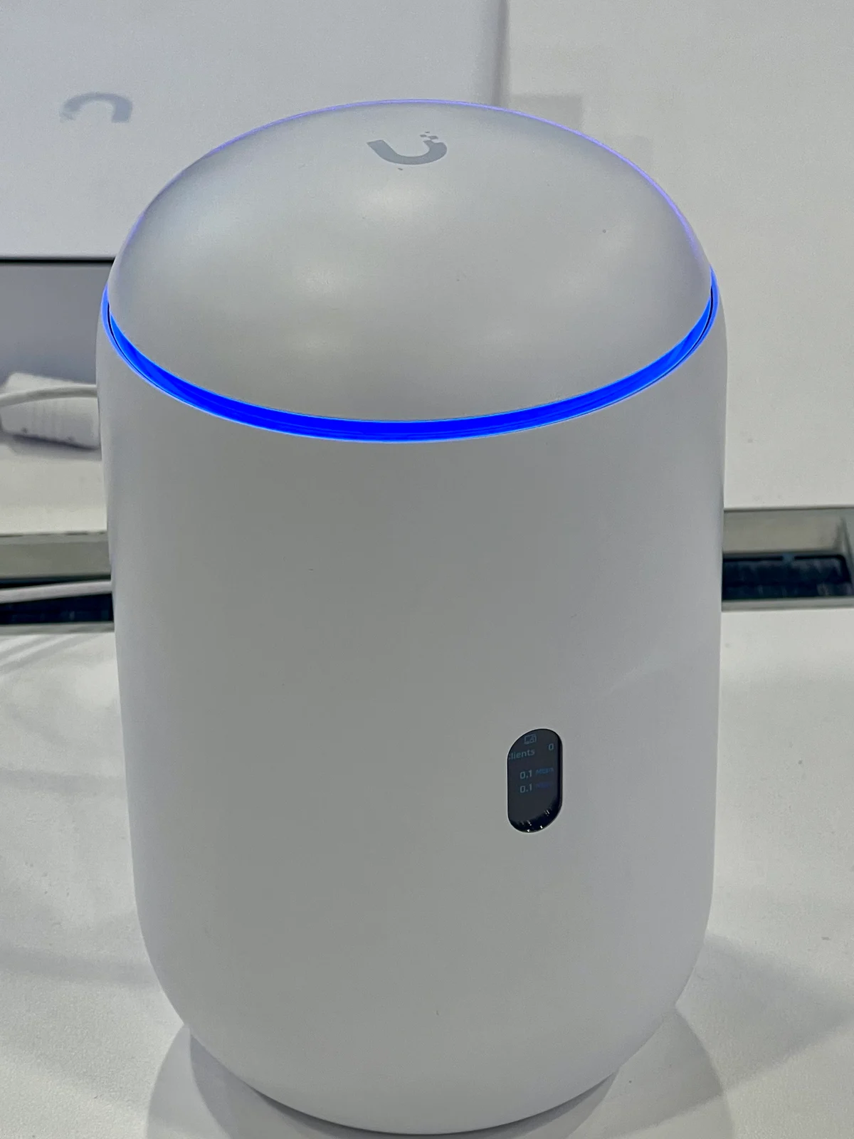 Roteador branco em formato de cúpula com anel de LED azul aceso, sobre uma mesa