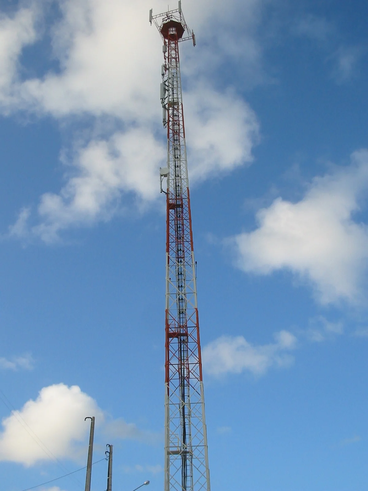 Torre de telefonia celular alta contra um céu azul com nuvens
