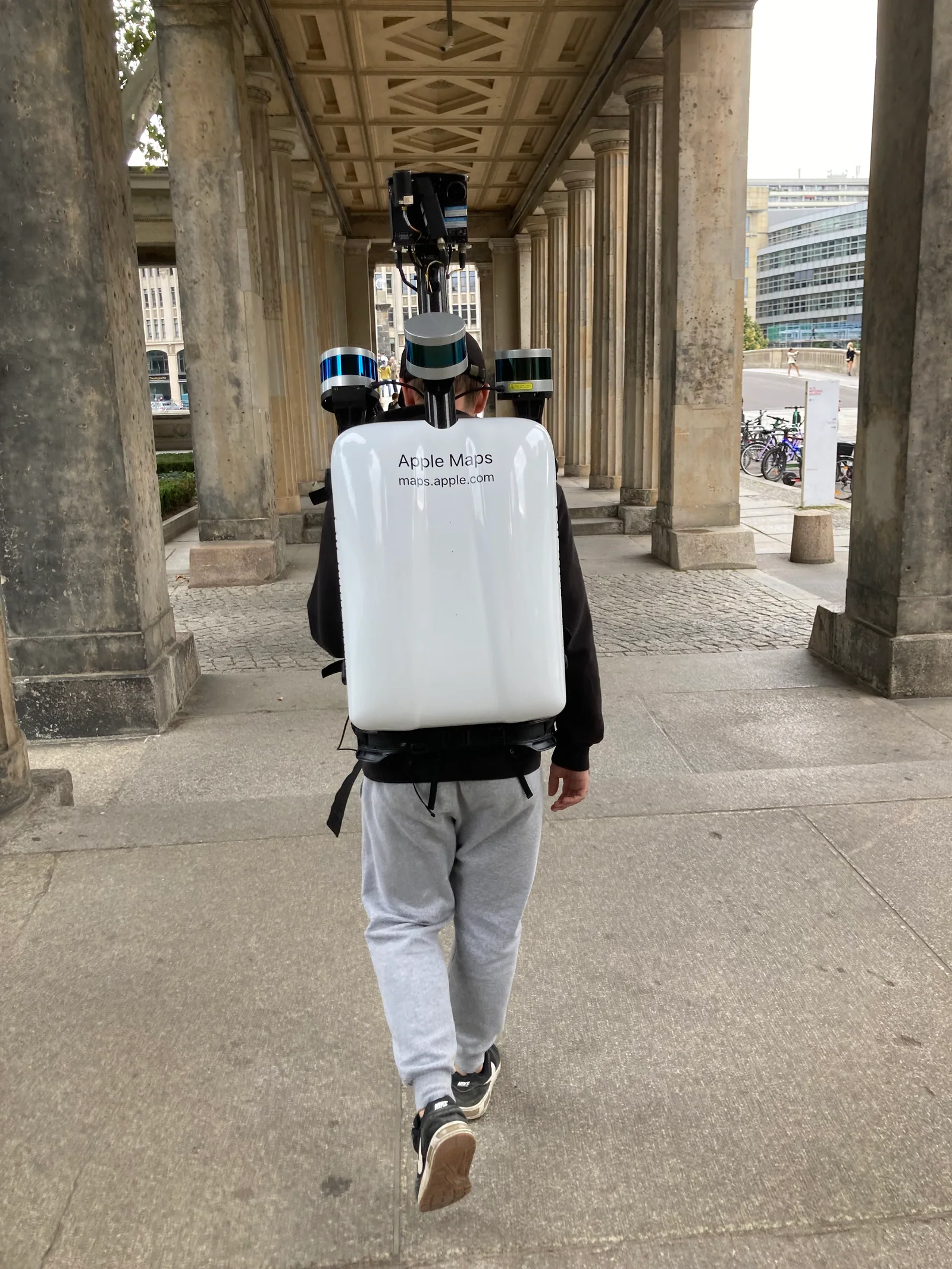 Vista traseira de operador com mochila branca identificada como Apple Maps em Berlim
