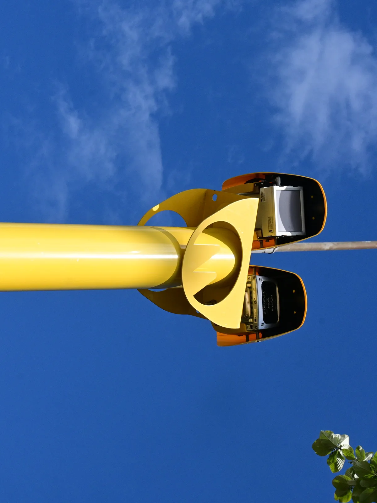 Close-up de câmera de fiscalização amarela instalada em poste, contra o céu azul
