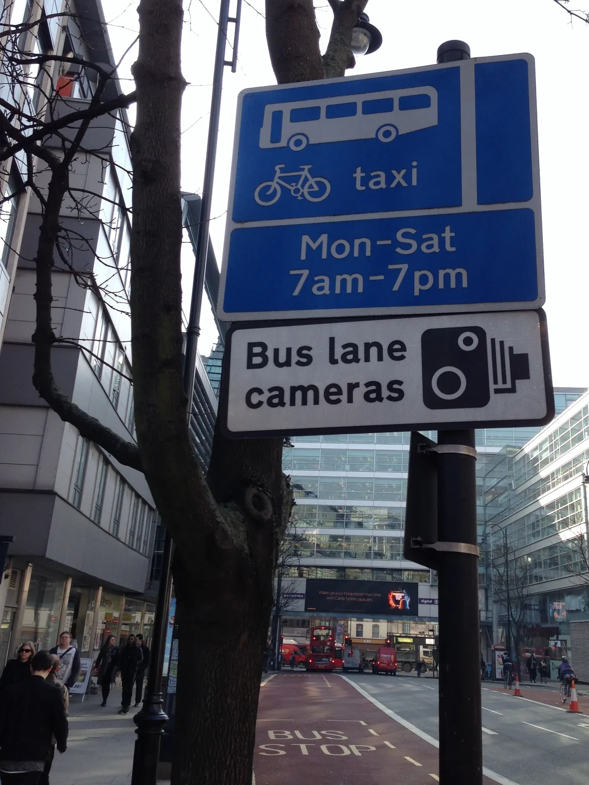 Placa de sinalização informando fiscalização por câmeras em faixa exclusiva de ônibus, em rua urbana