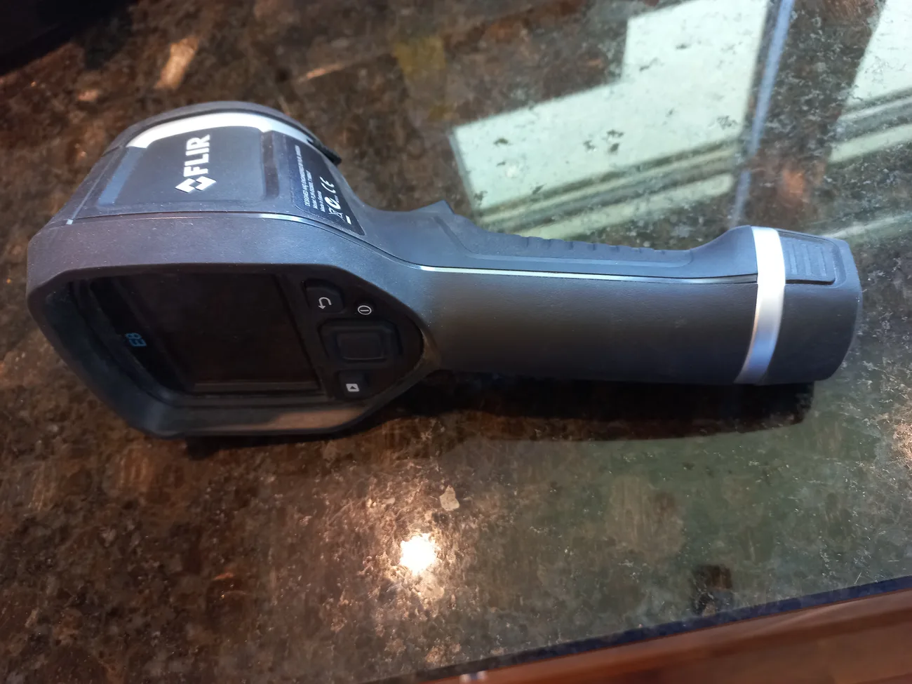 Câmera térmica portátil de mão, modelo FLIR, sobre uma bancada