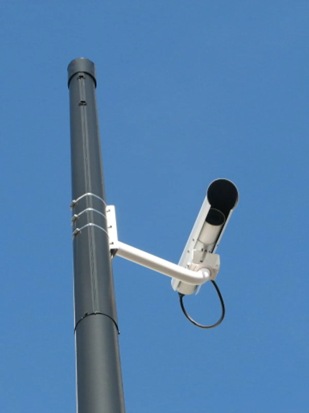 Câmera de segurança tipo bullet montada em um braço de suporte, no topo de um poste, contra o céu azul