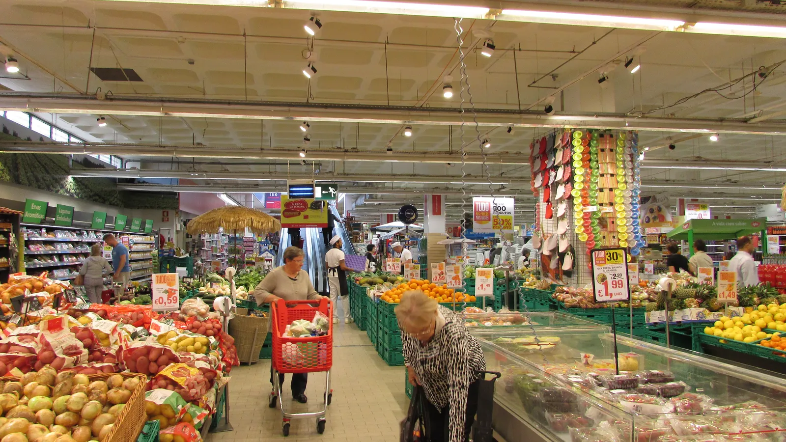 Corredor de supermercado com clientes fazendo compras entre prateleiras de frutas e verduras