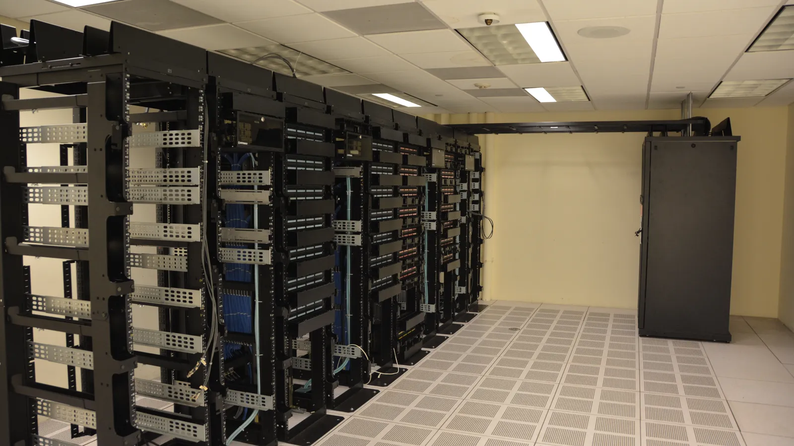 Sala de servidores com fileiras de racks de rede e cabeamento organizado, sem identificação de marca