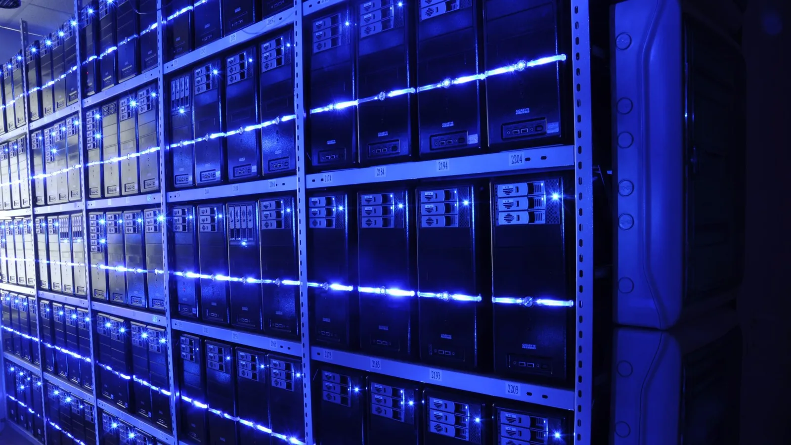 Corredor de data center com fileiras de servidores empilhados em racks metálicos, iluminados por luzes azuis de status