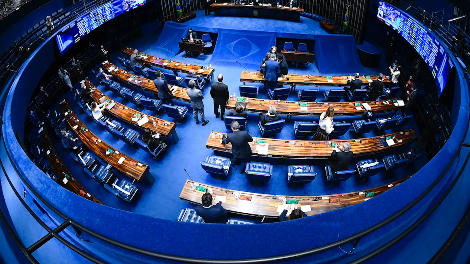Vista do alto do plenário do Senado Federal durante sessão, com senadores nas bancadas em semicírculo e painéis eletrônicos de votação nas laterais
