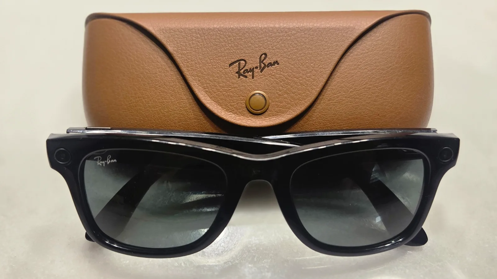 Óculos inteligentes Ray-Ban Meta Gen 1 de armação preta brilhante posicionados ao lado do estojo de couro marrom de carregamento