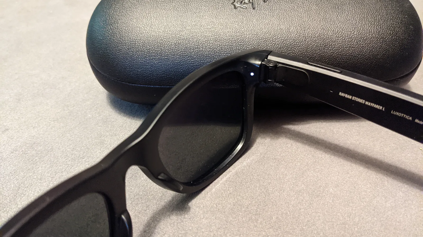 Óculos Ray-Ban Stories, geração anterior da parceria Meta, com o LED branco de aviso aceso ao lado da câmera, e o estojo de carregamento ao fundo