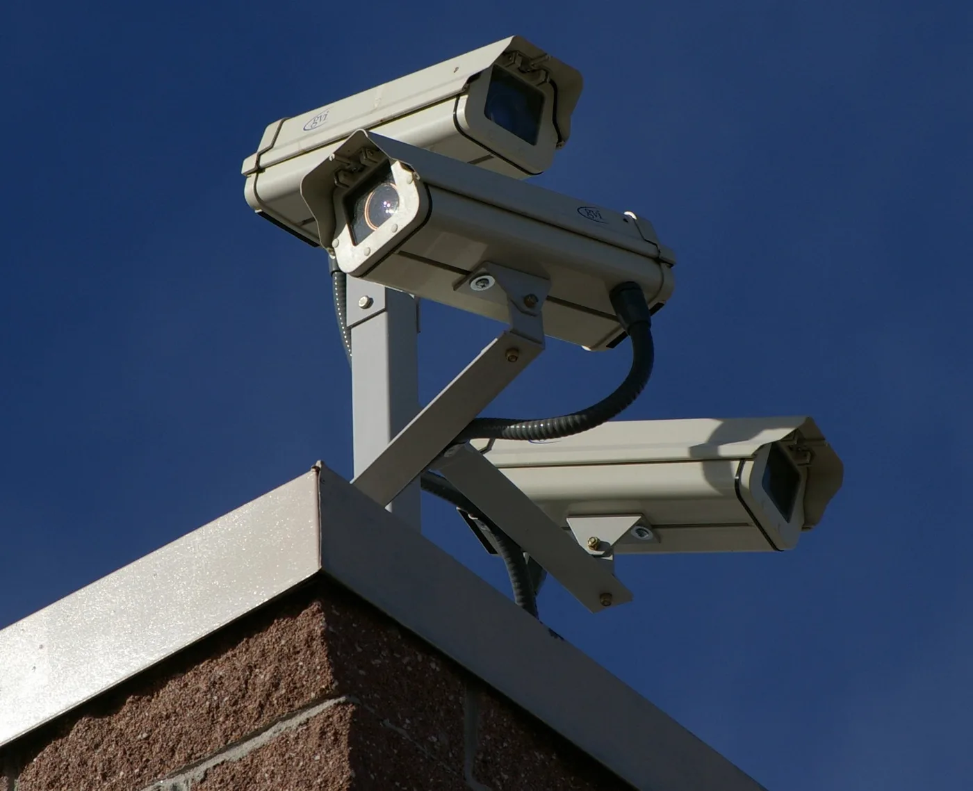 Três câmeras de CFTV instaladas no topo de uma fachada, contra o céu azul