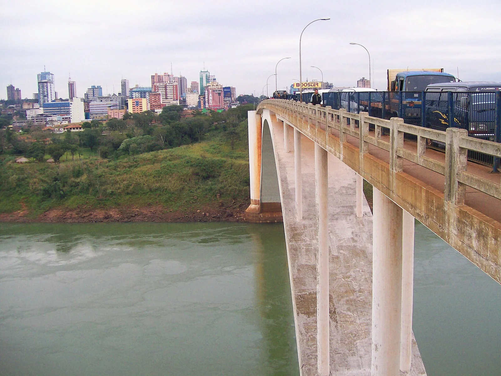 Ponte da Amizade sobre o rio Paraná, com ônibus e caminhões atravessando, e a cidade de Ciudad del Este ao fundo