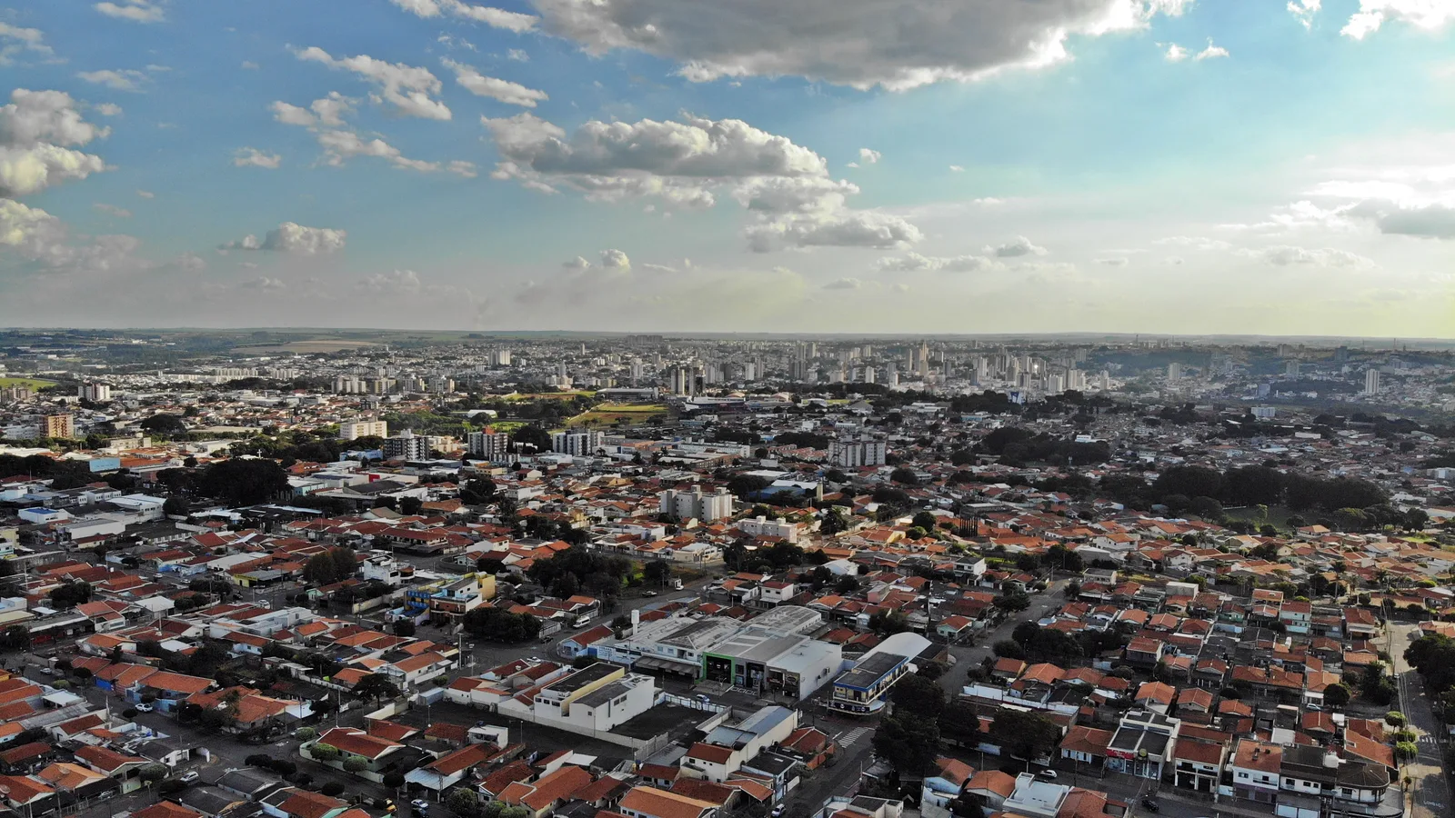 Vista aérea de Americana ao entardecer, mostrando bairros residenciais com telhados de telha cerâmica em primeiro plano e a região central da cidade ao fundo