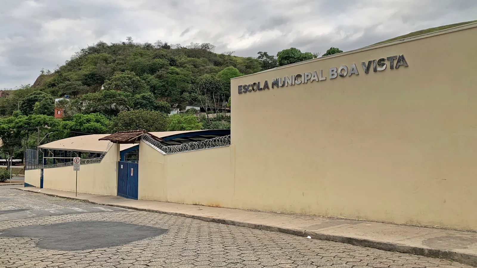 Fachada de escola municipal com muro alto e cerca de arame farpado