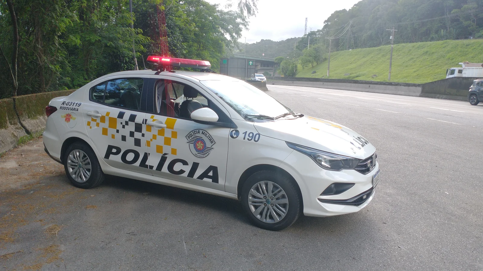 Viatura policial branca com faixas de identificação estacionada em via pública